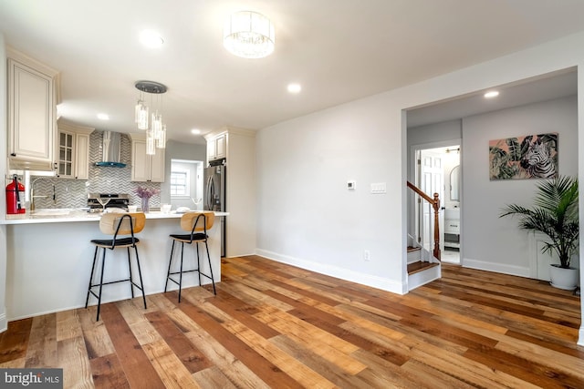 kitchen featuring a peninsula, wall chimney range hood, light countertops, stainless steel range oven, and light wood finished floors