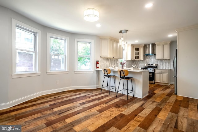 kitchen with a peninsula, wall chimney range hood, a kitchen bar, tasteful backsplash, and appliances with stainless steel finishes