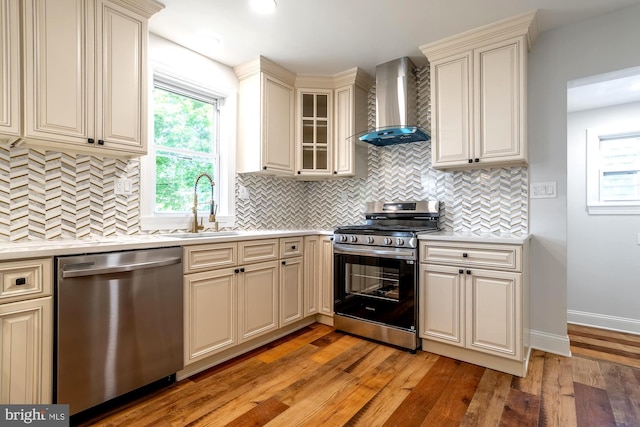 kitchen featuring wall chimney range hood, appliances with stainless steel finishes, light countertops, and cream cabinetry