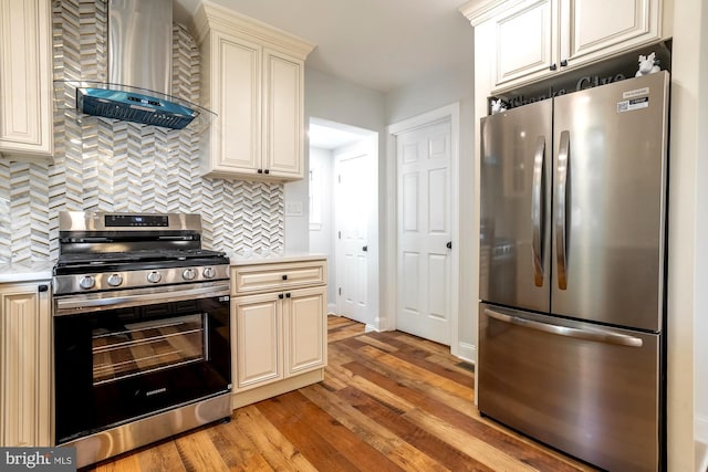kitchen featuring light countertops, cream cabinets, stainless steel appliances, and wall chimney exhaust hood