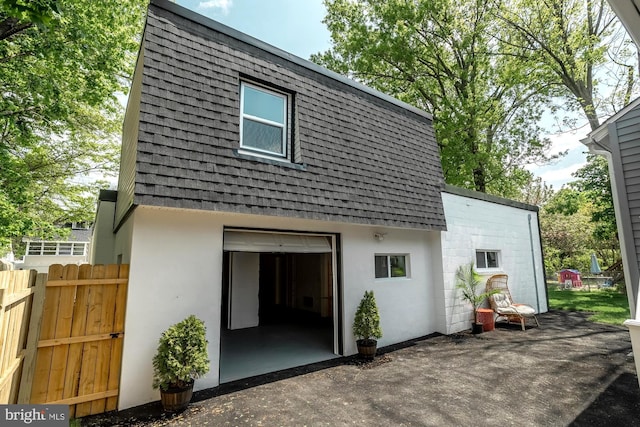 back of property with fence, a shingled roof, stucco siding, a patio area, and mansard roof