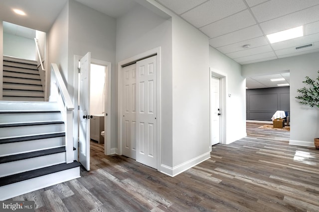 foyer with a paneled ceiling, baseboards, wood finished floors, visible vents, and stairway