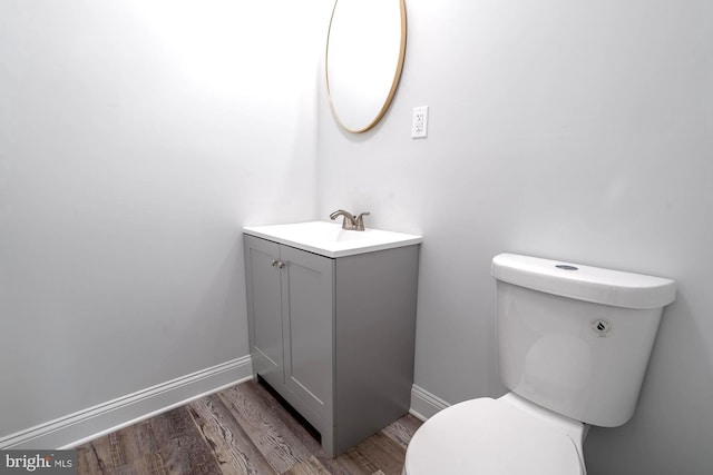 half bathroom featuring vanity, baseboards, toilet, and wood finished floors