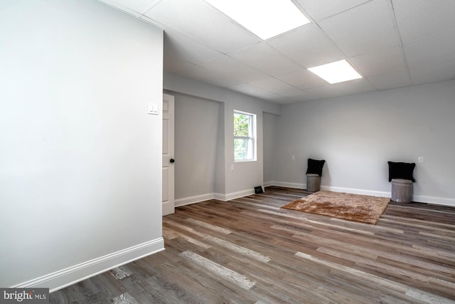 unfurnished living room featuring baseboards, a drop ceiling, and wood finished floors