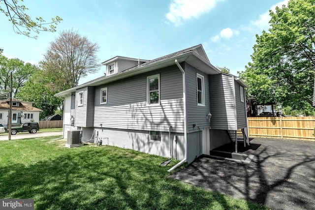 view of side of property featuring central AC, fence, and a yard