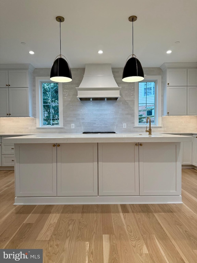 kitchen with light wood-style floors, light countertops, custom range hood, a sink, and backsplash