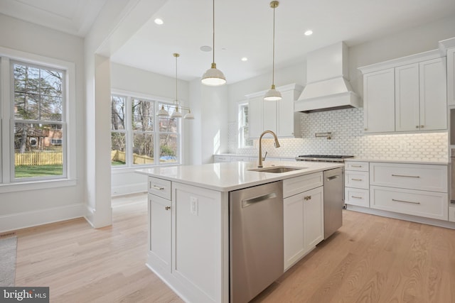 kitchen with a kitchen island with sink, appliances with stainless steel finishes, a sink, premium range hood, and white cabinets