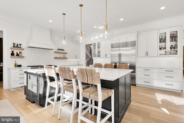 kitchen with white cabinets, open shelves, stainless steel built in fridge, and premium range hood