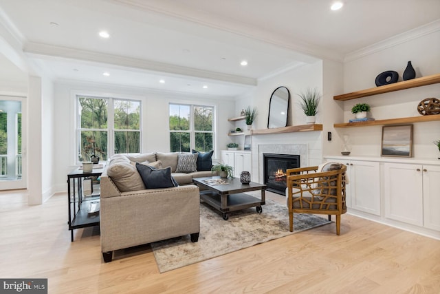 living room with recessed lighting, ornamental molding, light wood-style flooring, and a glass covered fireplace