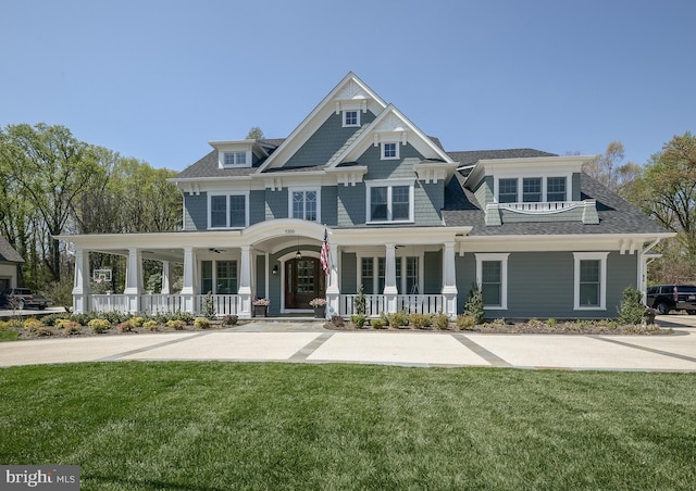 view of front facade featuring a ceiling fan, covered porch, a shingled roof, and a front lawn