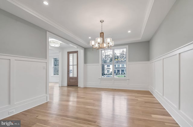 unfurnished dining area featuring light wood-type flooring, a wainscoted wall, a notable chandelier, ornamental molding, and a decorative wall