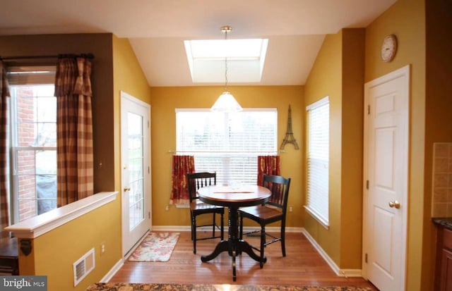 dining room with visible vents, plenty of natural light, wood finished floors, and vaulted ceiling with skylight