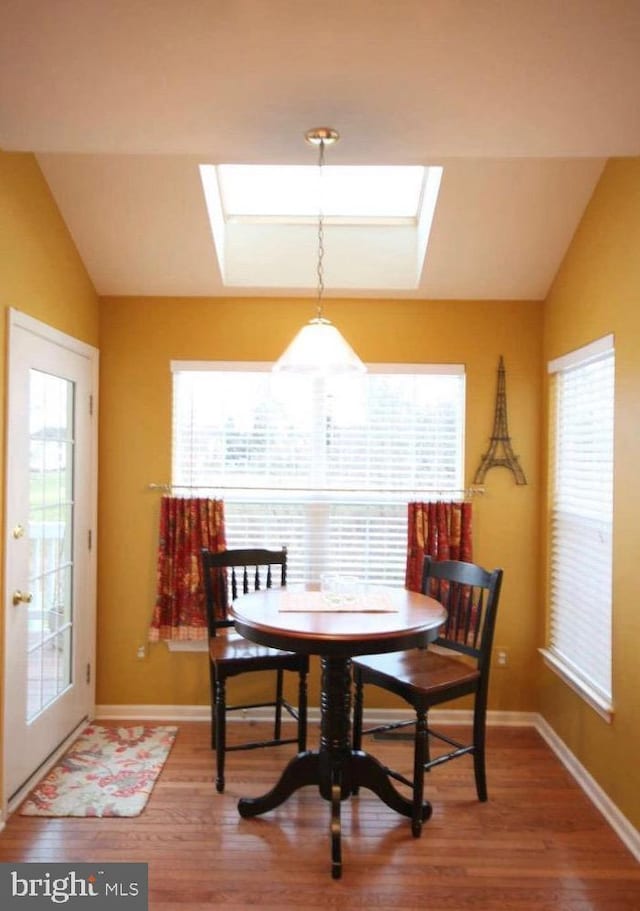 dining room with baseboards, wood finished floors, and vaulted ceiling with skylight