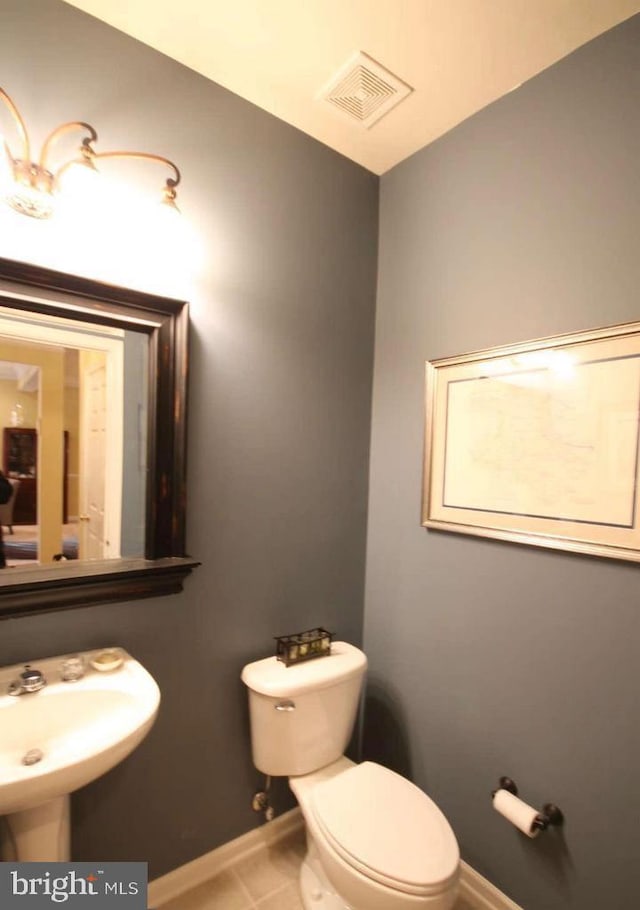 half bathroom with visible vents, tile patterned flooring, toilet, baseboards, and a sink