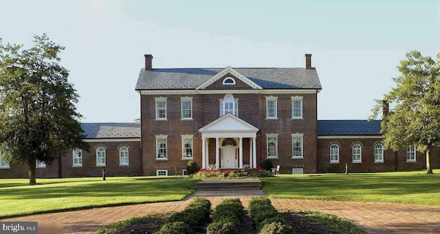 colonial-style house with brick siding, a chimney, and a front lawn