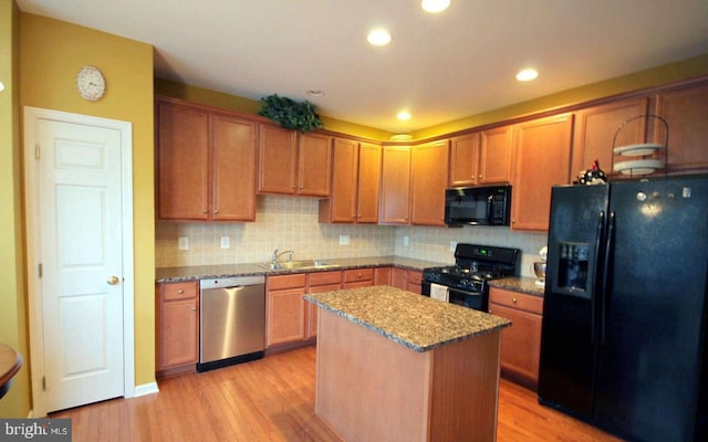 kitchen with stone counters, a kitchen island, black appliances, and light wood finished floors