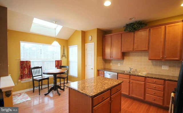 kitchen with stone countertops, lofted ceiling with skylight, a sink, light wood-style flooring, and backsplash