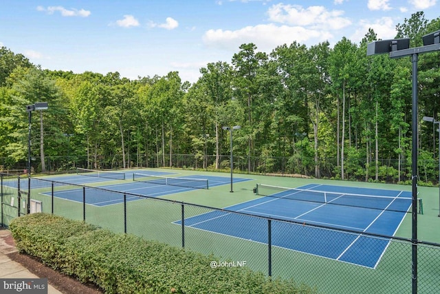 view of tennis court with a view of trees, fence, and community basketball court