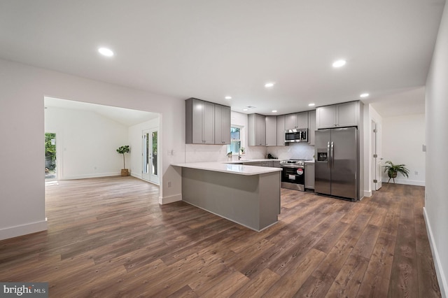 kitchen featuring appliances with stainless steel finishes, light countertops, gray cabinets, a peninsula, and dark wood-style floors