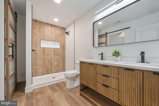 full bath featuring toilet, tiled shower, a sink, and wood finished floors