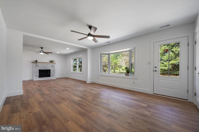 unfurnished living room featuring ceiling fan, a fireplace, dark wood finished floors, baseboards, and visible vents