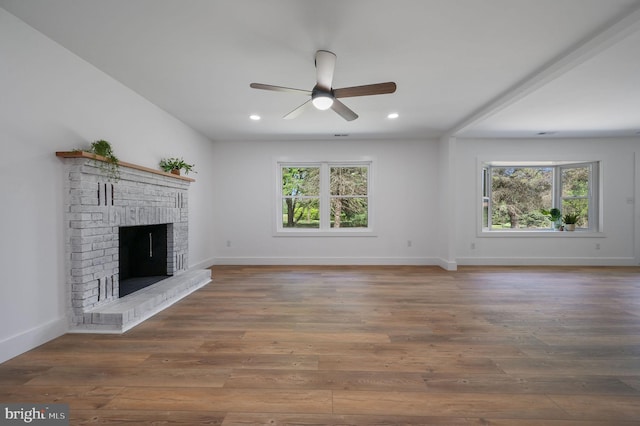unfurnished living room featuring a brick fireplace, ceiling fan, plenty of natural light, and wood finished floors