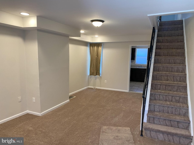 finished below grade area with visible vents, a sink, carpet floors, baseboards, and stairs