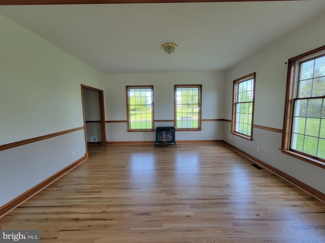 empty room featuring baseboards, plenty of natural light, a wood stove, and light wood-style floors