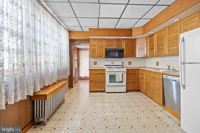 kitchen with a sink, white appliances, light countertops, a paneled ceiling, and light floors