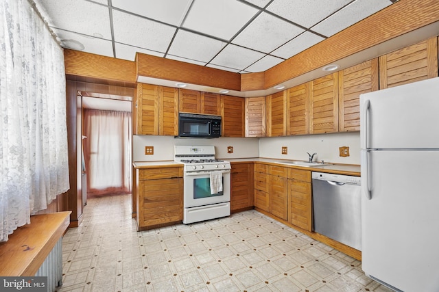 kitchen featuring white appliances, a paneled ceiling, a sink, and light floors