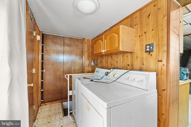 washroom with wooden walls, light floors, cabinet space, and washer and clothes dryer