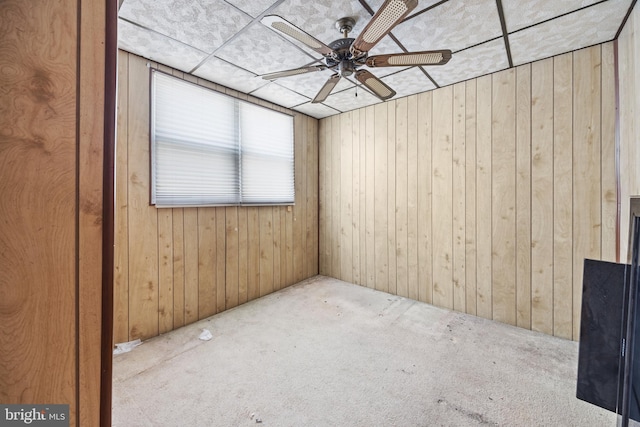 unfurnished room featuring ceiling fan, wood walls, and carpet