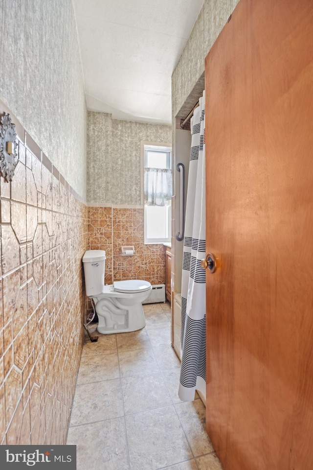 bathroom featuring a shower with shower curtain, baseboard heating, toilet, and tile walls