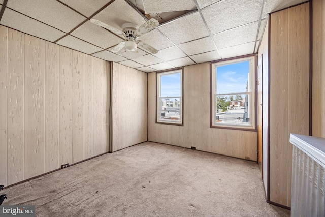 carpeted spare room with wood walls, a paneled ceiling, and ceiling fan