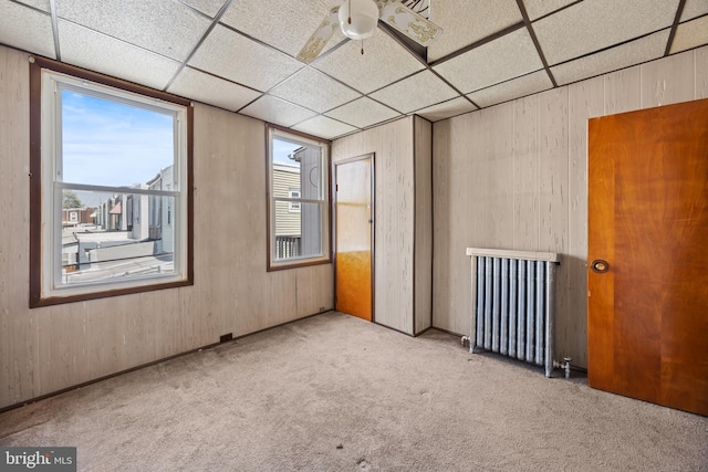 carpeted empty room featuring a paneled ceiling, ceiling fan, and radiator heating unit
