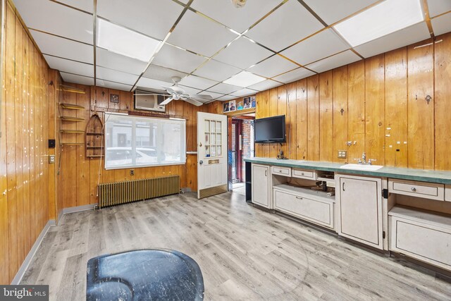 kitchen featuring a sink, radiator, a drop ceiling, and wooden walls