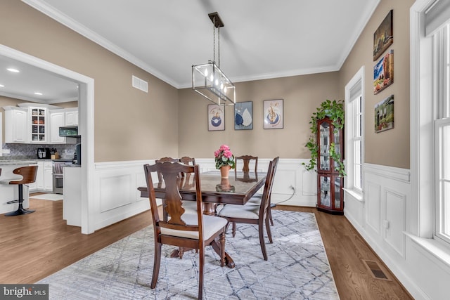 dining room with ornamental molding, light wood-style flooring, visible vents, and a wainscoted wall