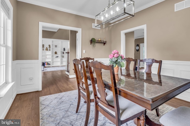dining area featuring ornamental molding, a wainscoted wall, visible vents, and wood finished floors