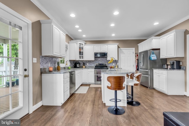 kitchen with a breakfast bar, ornamental molding, white cabinetry, backsplash, and appliances with stainless steel finishes
