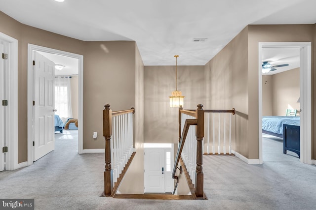 hall with baseboards, an upstairs landing, visible vents, and carpet floors