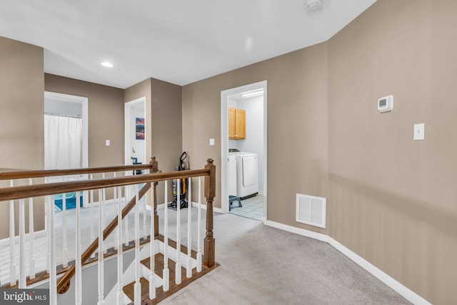 hall featuring washer and clothes dryer, an upstairs landing, visible vents, light carpet, and baseboards