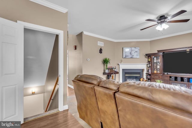 living room featuring a glass covered fireplace, ornamental molding, light wood-style flooring, and ceiling fan