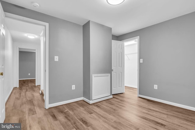 unfurnished bedroom featuring light wood-type flooring, baseboards, and a spacious closet