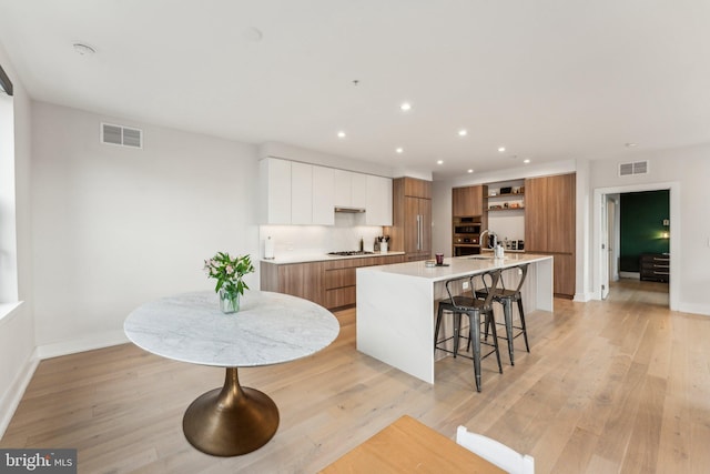 kitchen with modern cabinets, open shelves, brown cabinets, an island with sink, and a kitchen bar