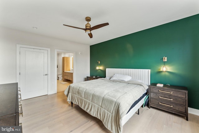 bedroom featuring light wood finished floors, ensuite bath, and ceiling fan