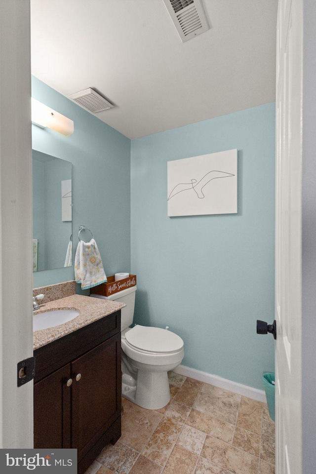 half bathroom featuring stone finish flooring, toilet, visible vents, and vanity
