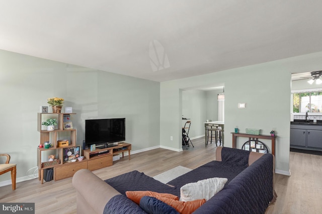 living room featuring light wood-style floors, baseboards, and ceiling fan