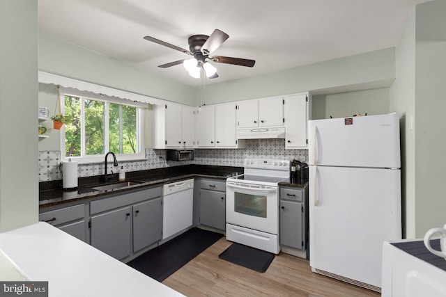 kitchen with white appliances, backsplash, under cabinet range hood, and a sink