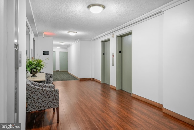 hall featuring ornamental molding, elevator, a textured ceiling, and wood finished floors
