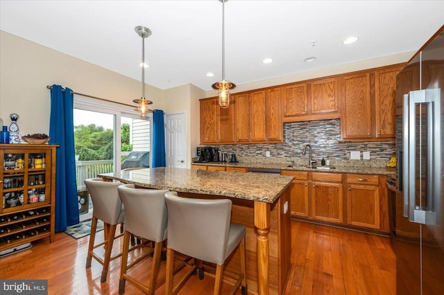 kitchen with a sink, brown cabinetry, high end refrigerator, a center island, and tasteful backsplash